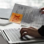 Individual working on tax paperwork and laptop, preparing to submit Form 4868 for a filing extension.