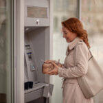 Mature woman using an ATM and putting her credit card away, reflecting everyday financial activity impacted by FATCA.