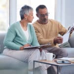 Senior couple sitting on the sofa reviewing bills and financial documents, illustrating how the windfall elimination provision can affect retirement planning decisions.