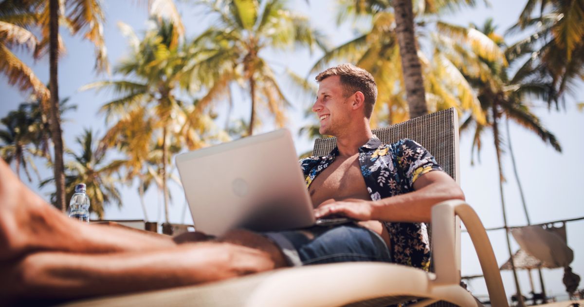 Best digital nomad jobs - man sitting under palm trees on a sunny day by the pool