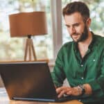 Stressed young man working on a laptop, capturing the pressure of wondering what happens if you miss the tax deadline.