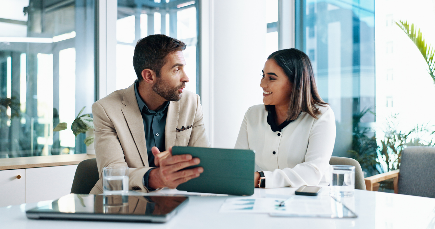Smiling professionals reviewing financial data on a tablet—collaborating on business and wealth management UK strategies.