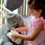 Little girl bandages a koala toy—playful look at healthcare in Australia.