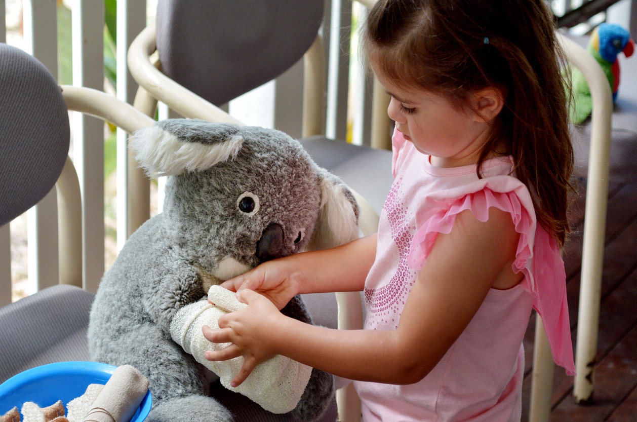 Little girl bandages a koala toy—playful look at healthcare in Australia.