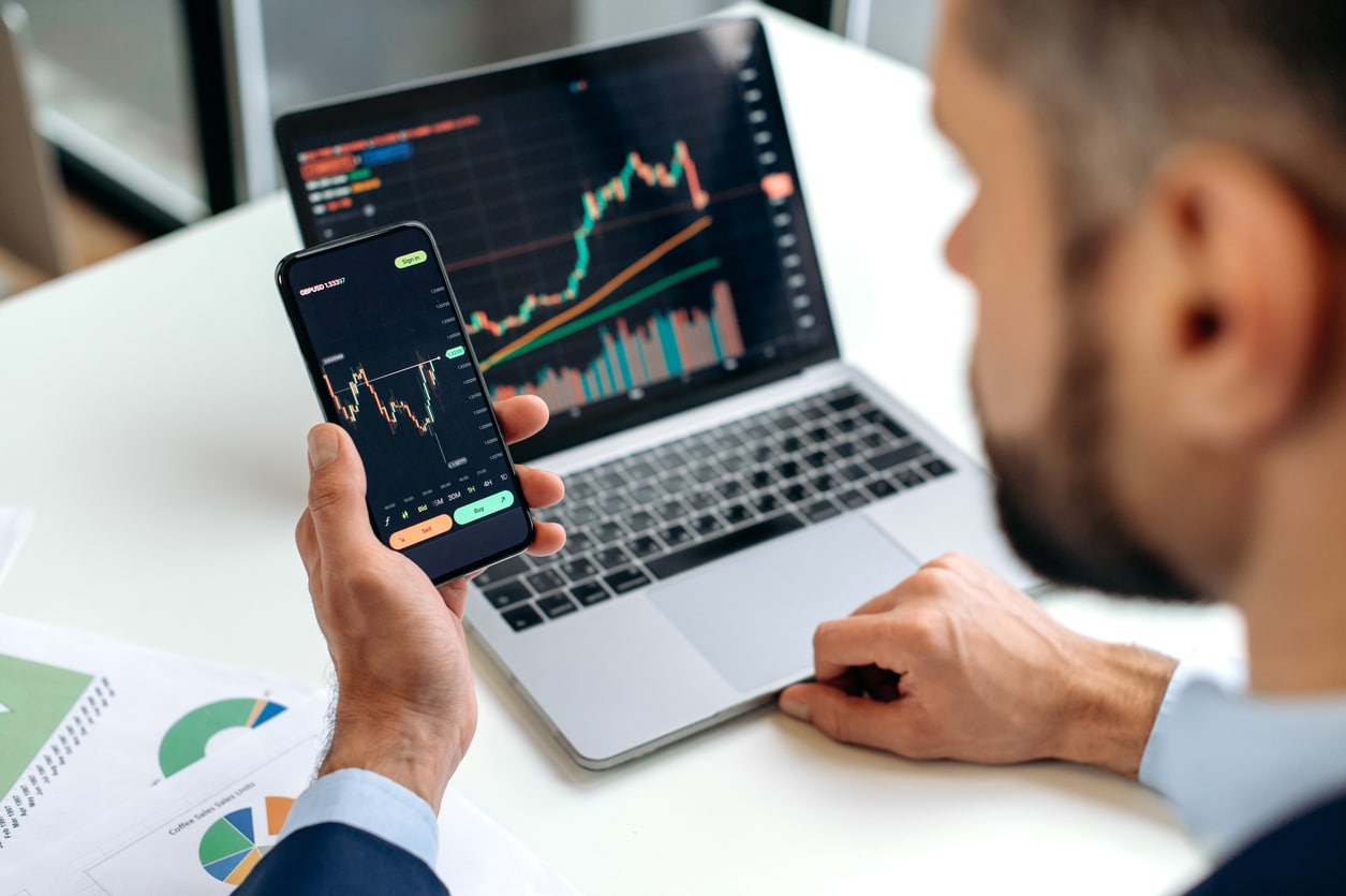 Hands holding a smartphone with a price chart, symbolizing cryptocurrency tax reporting.
